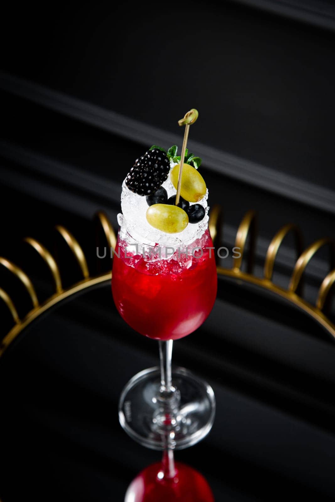 red cocktail in a transparent glass with round ice, whipped cream and black berry on top