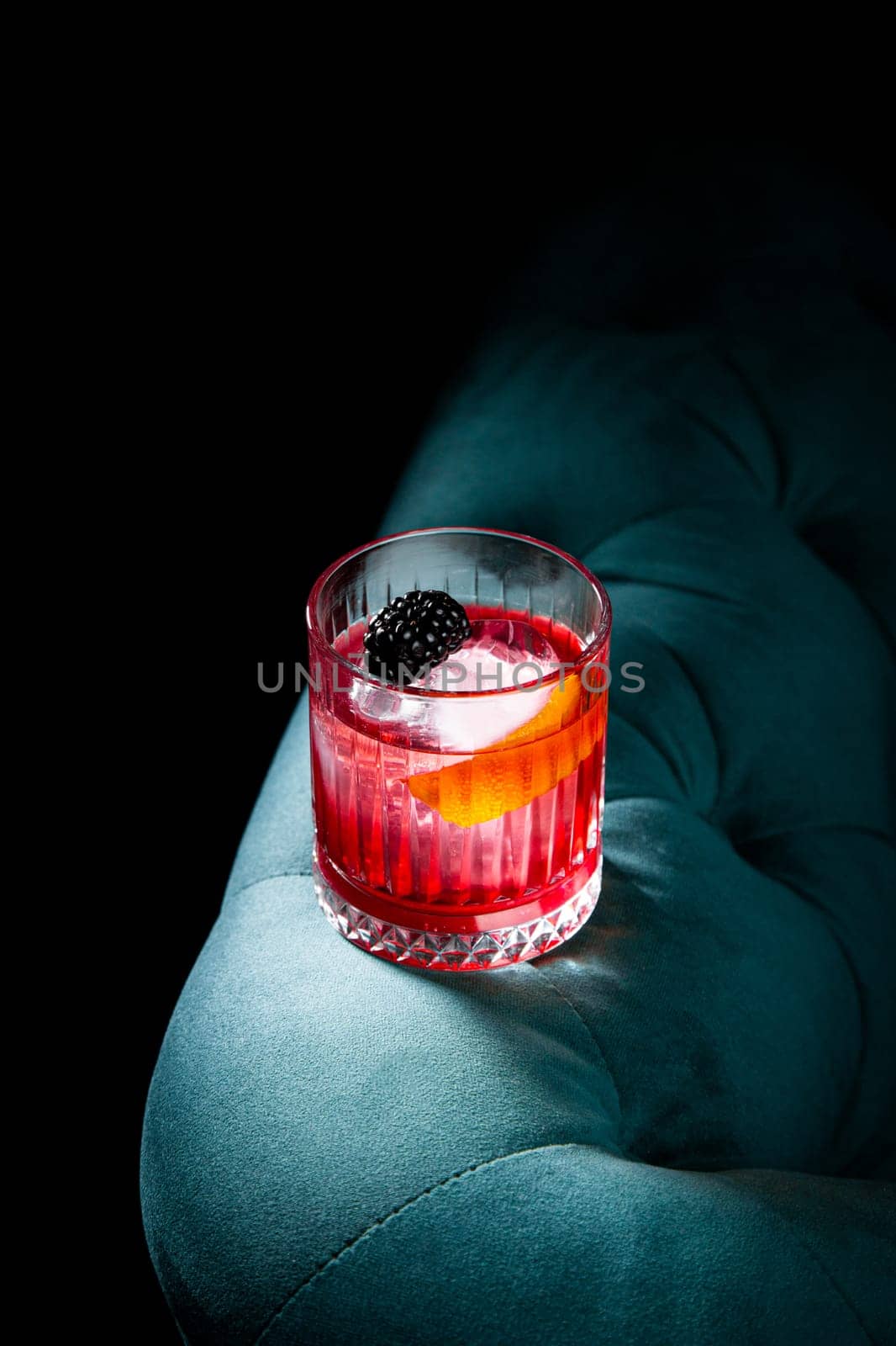 red cocktail in a transparent glass with round ice, whipped cream and black berry on top