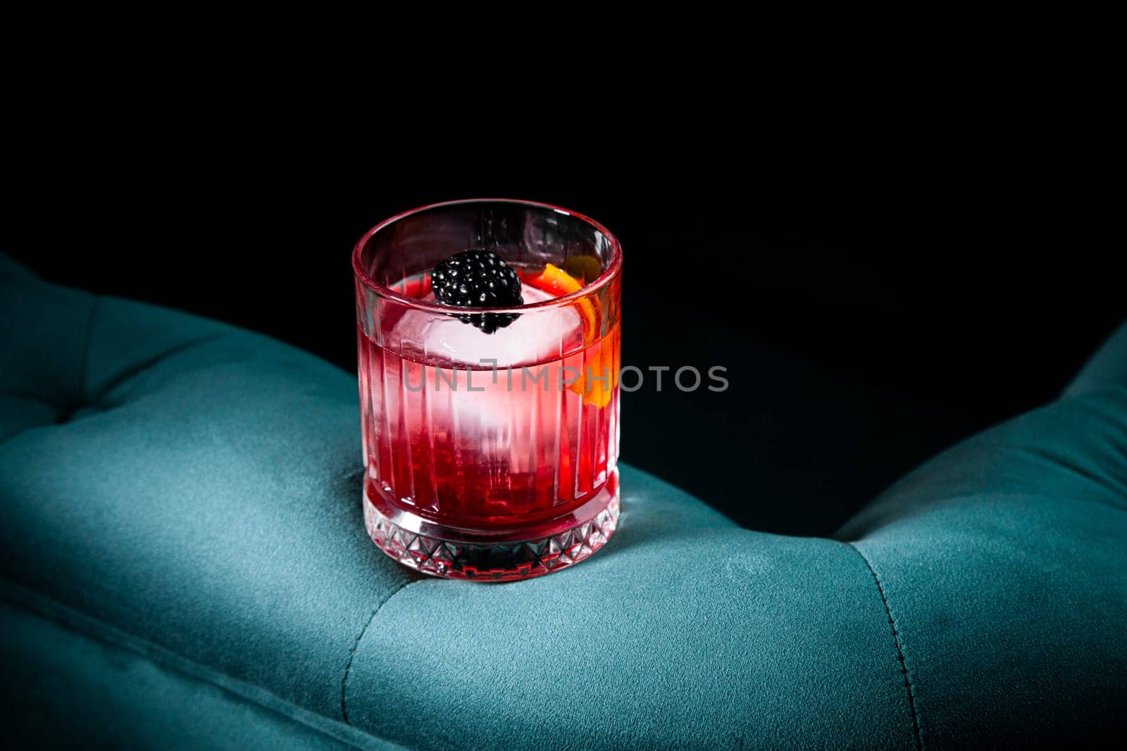red cocktail in a transparent glass with round ice, whipped cream and black berry on top