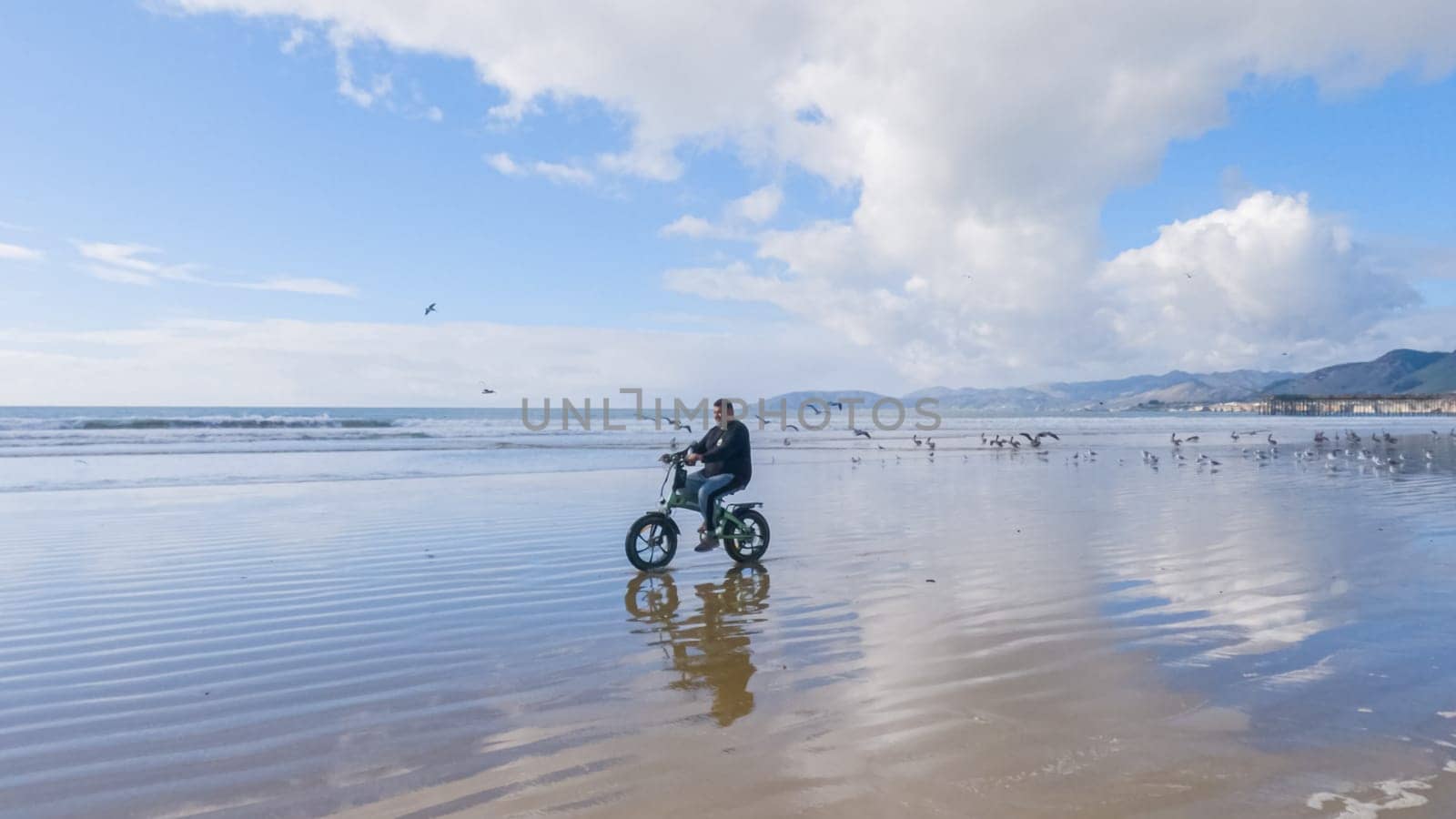 Pismo Beach, California, USA-December 5, 2022-Person enjoys a leisurely bike ride along the shoreline on a calm winter beach.