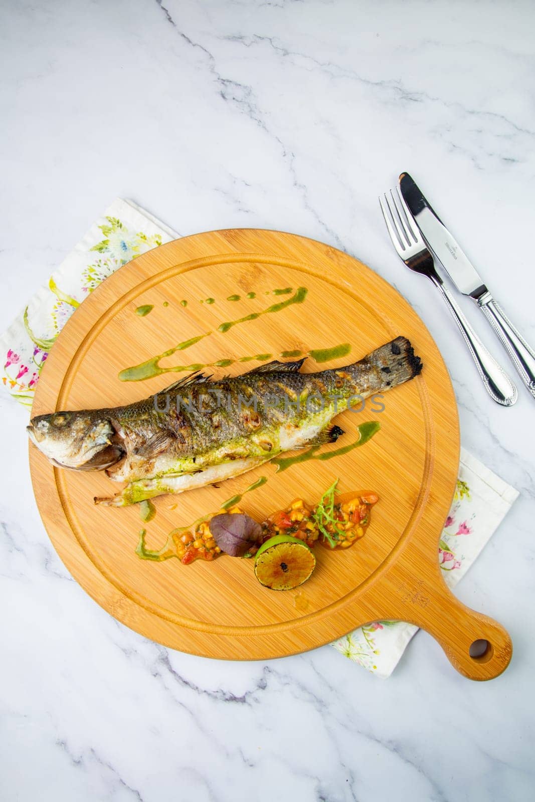 baked fish with lime and spices on a wooden tray on a marble background, top view by tewolf