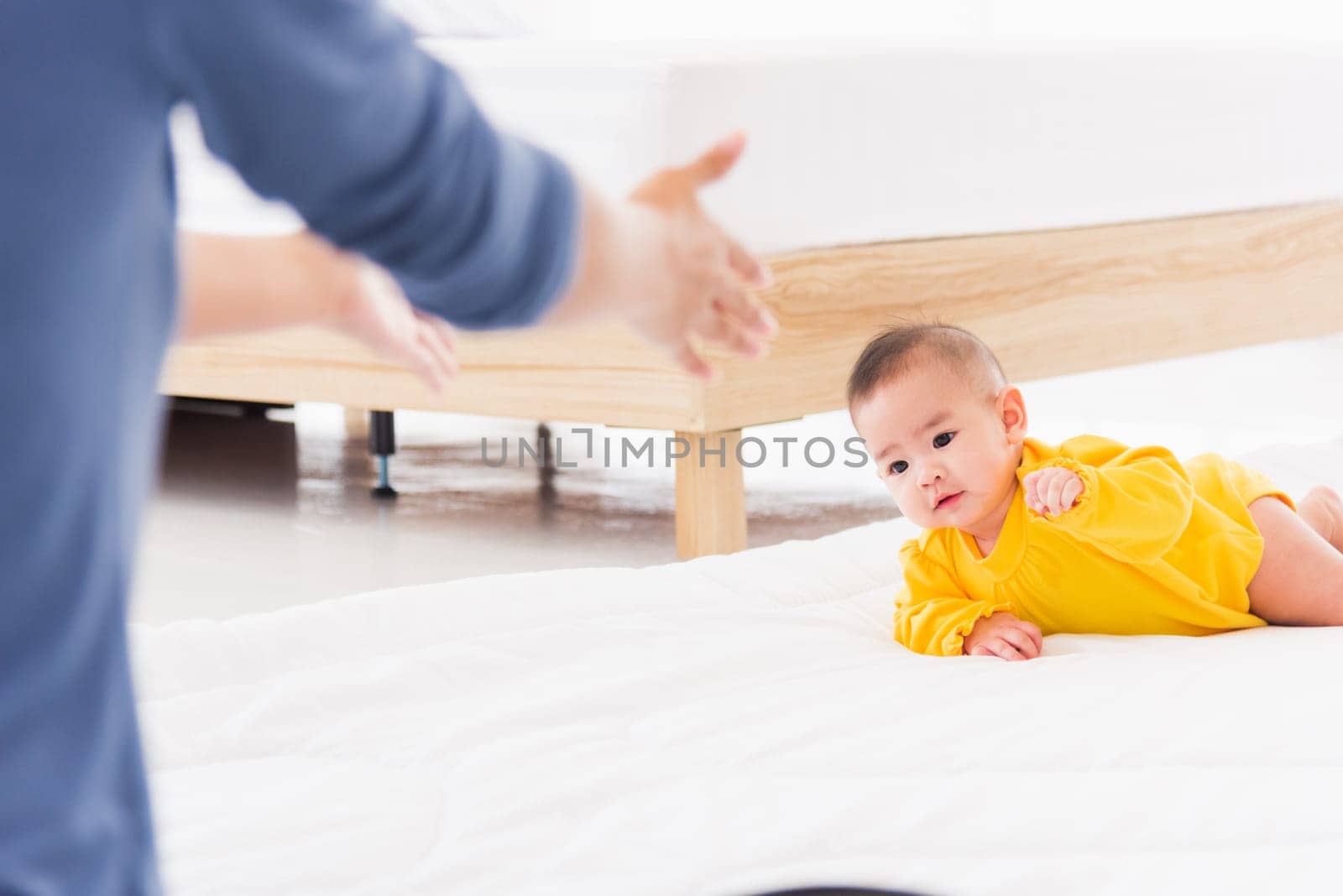 Asian happy young mother have fun learn walking crawling his daughter baby indoors bedroom at home. The mom playing with her little baby to crawl, two family