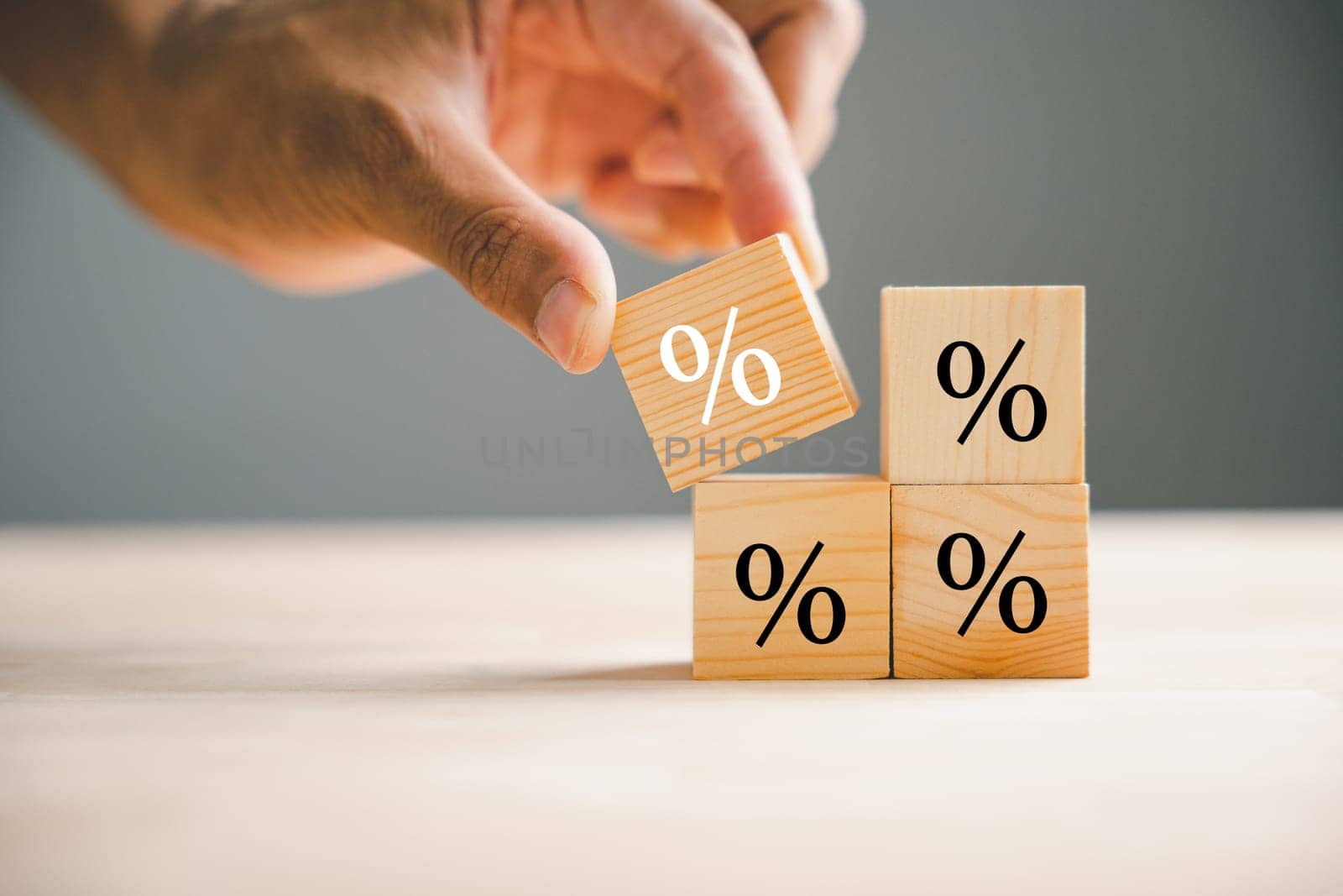 Concept of interest rate and financial rates. Hand placing a wooden cube block on top, symbolizing an increase, with an upward direction icon and percentage symbol.