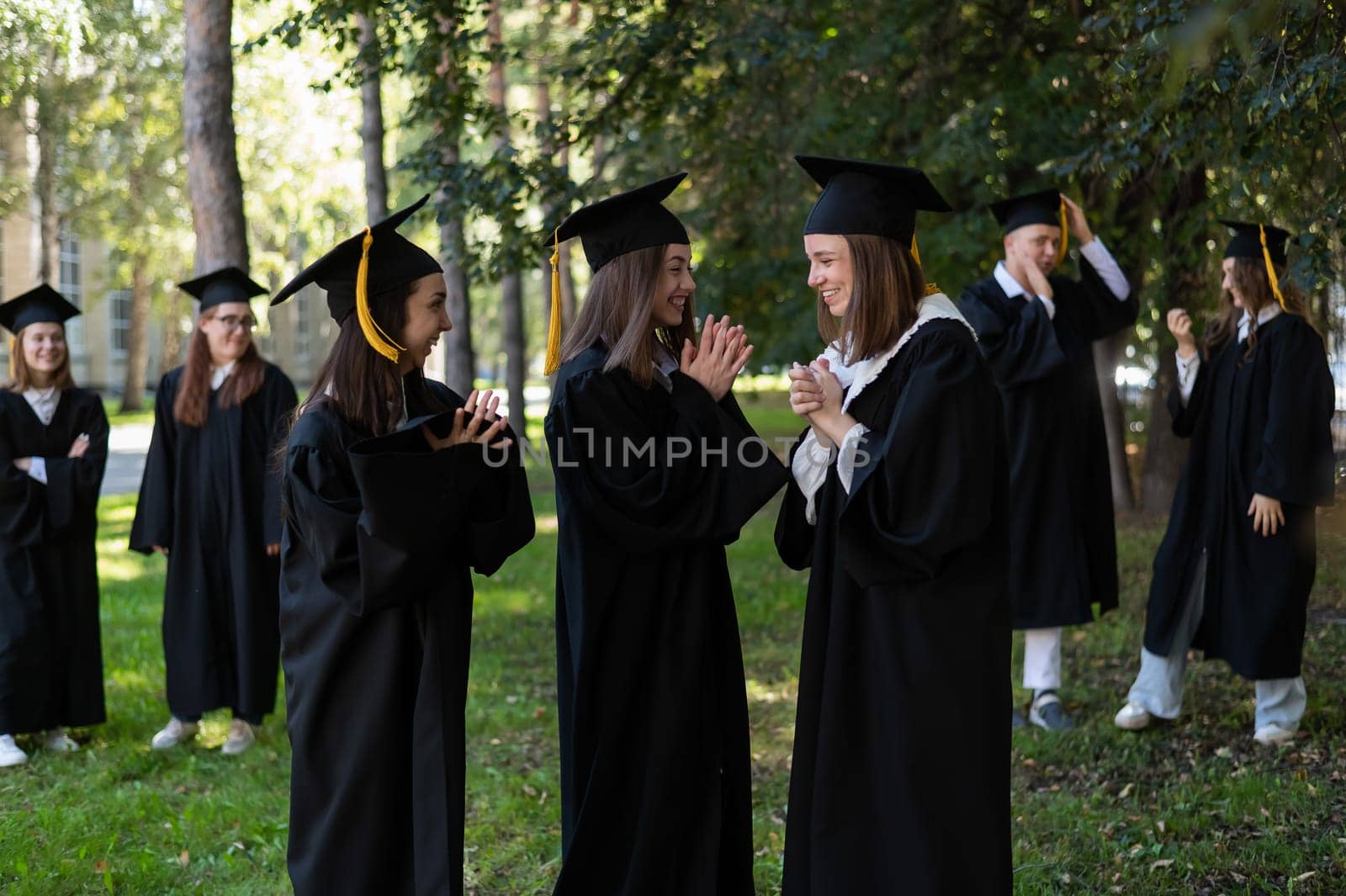 A group of graduates in robes congratulate each other on their graduation outdoors. by mrwed54