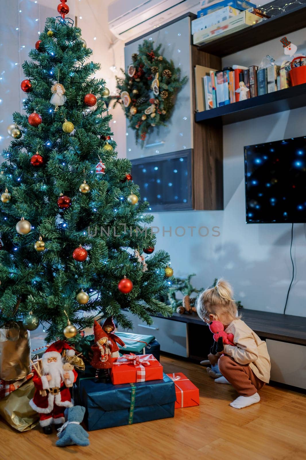 Little girl squats looking at gifts under the tree. Back view. High quality photo