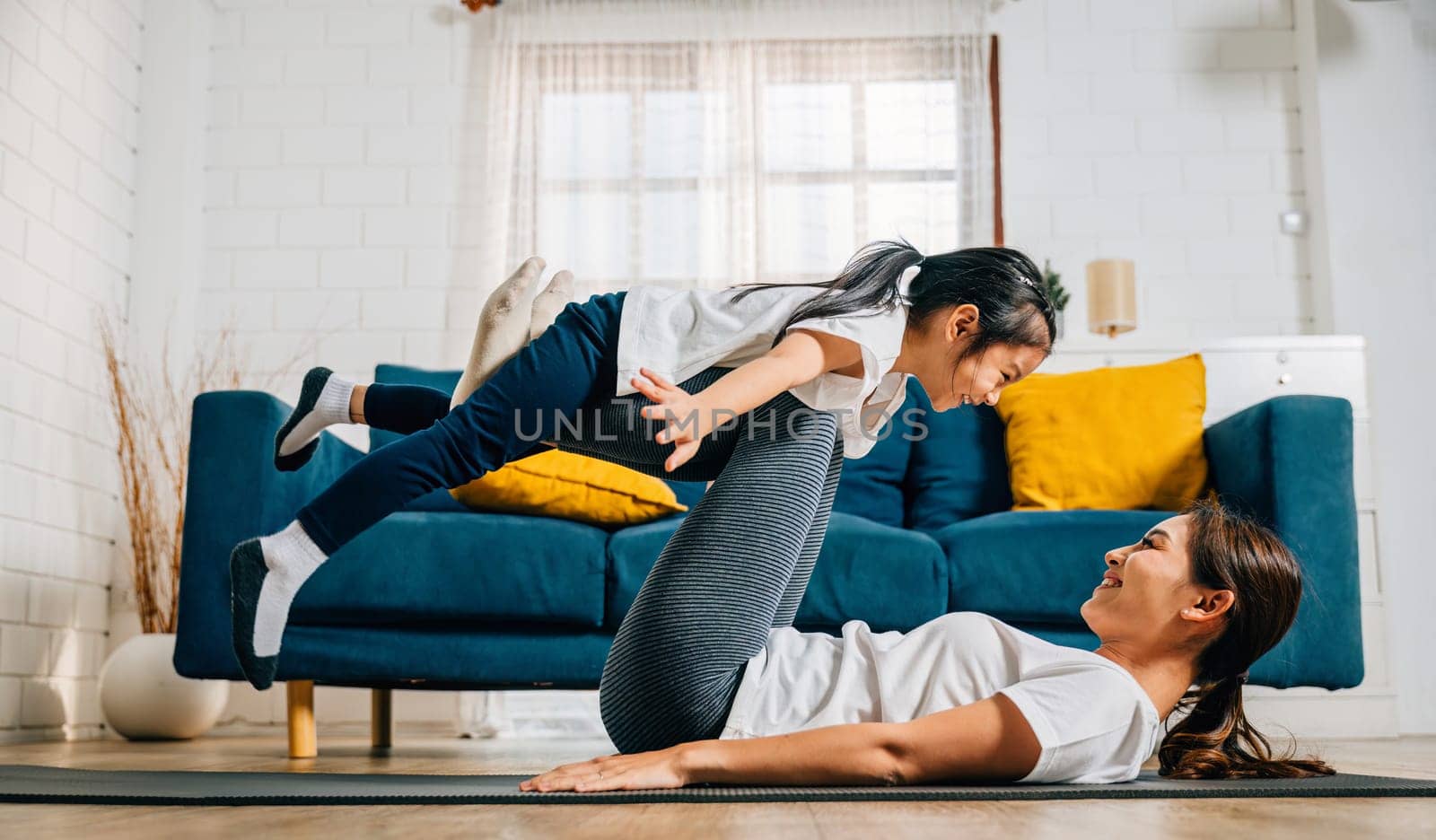 A mother and her daughter find delight in a family yoga moment playfully pretending to 'fly' like airplanes nurturing trust harmony and happiness in their cherished relationship.