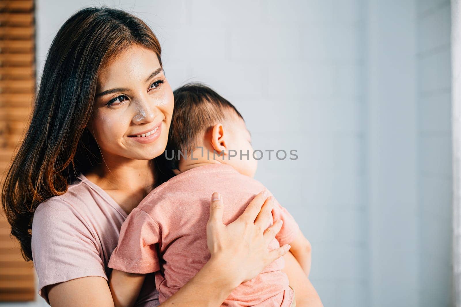 A tender loving biracial mother cradles her small sleeping newborn in her arms by Sorapop