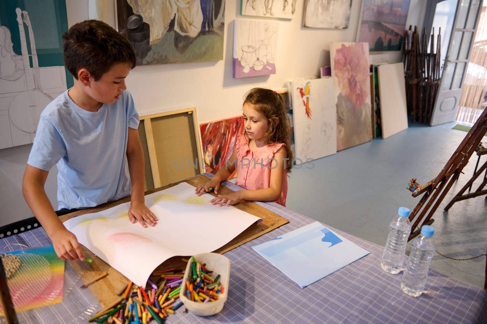 Adorable diverse children, a teenage boy and preschool girl drawing on white paper sheet during art class. People. Kids and hobbies.