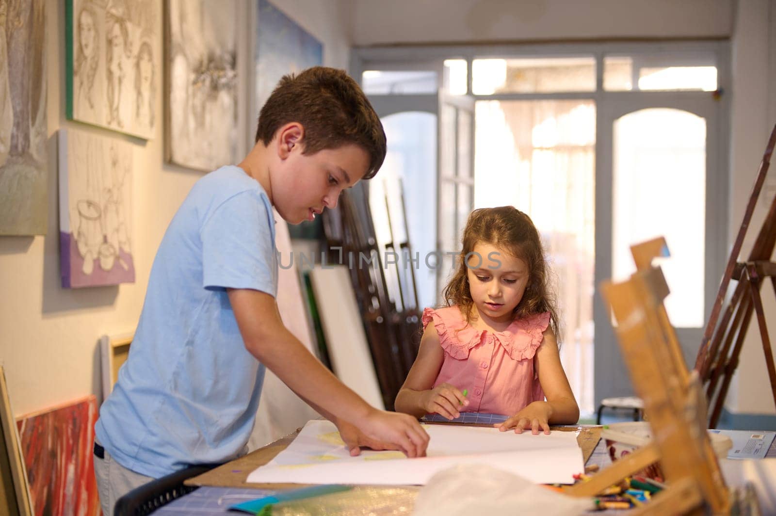 Two adorable kids, teenage boy and his younger sister, a little girl drawing, learning art in creative workshop. People. Childhood. Kids entertainment and development of creative skills in art gallery