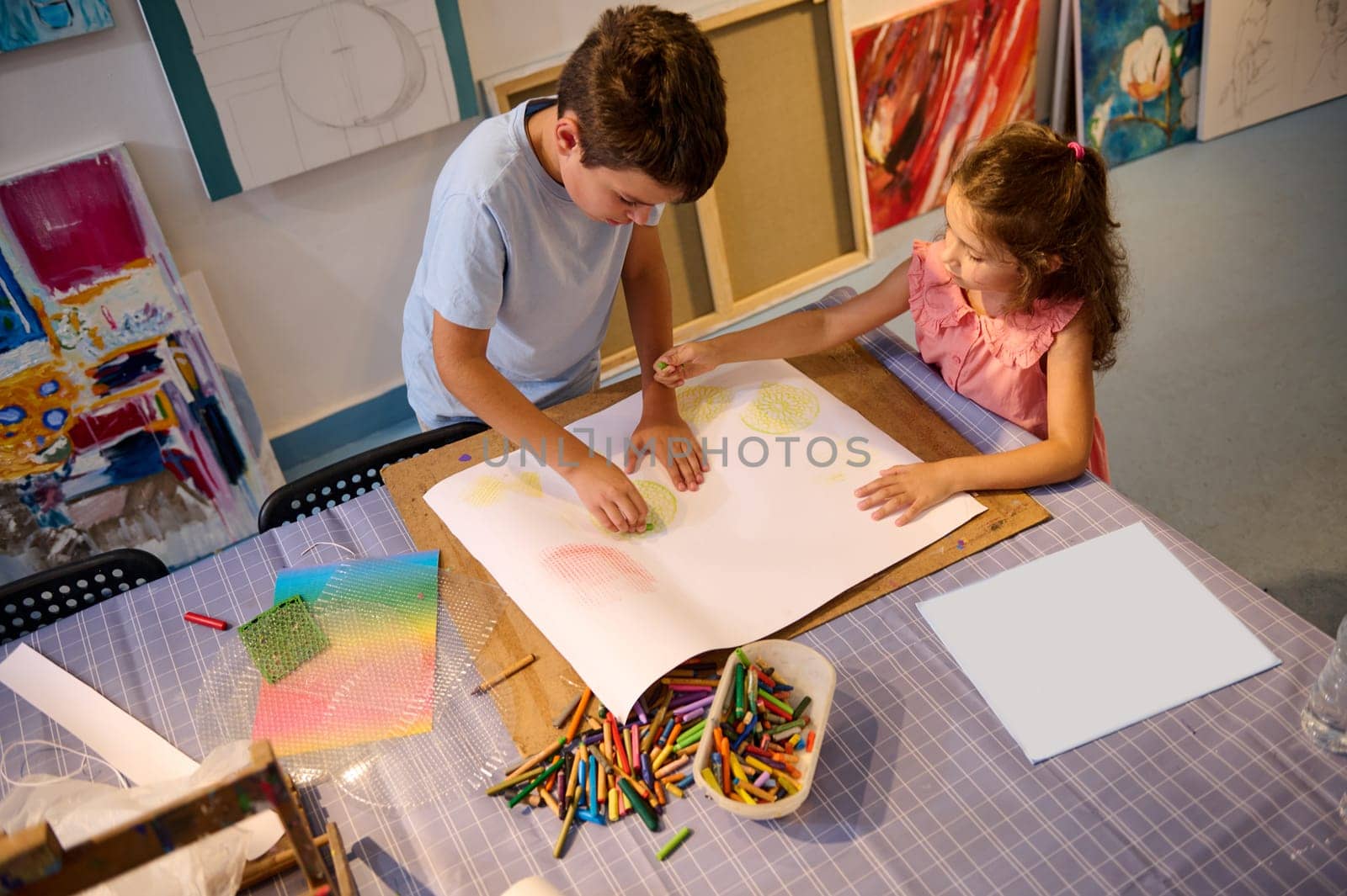 Top view of creative kids during an art class in a daycare center or elementary school classroom drawing with female teacher. People. Entertainment for children. Fine and visual art concept. Leisure