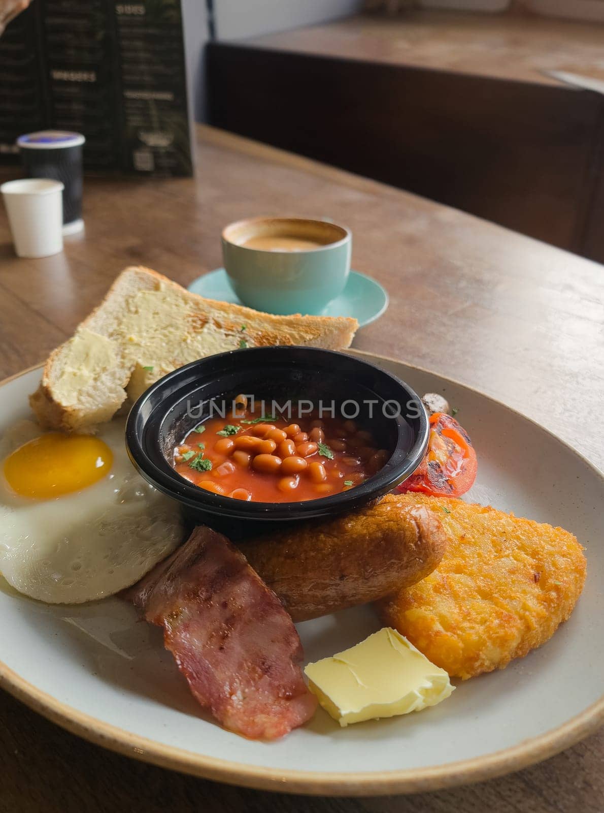 Full English breakfast with beans and sausage served on wooden table in pub
