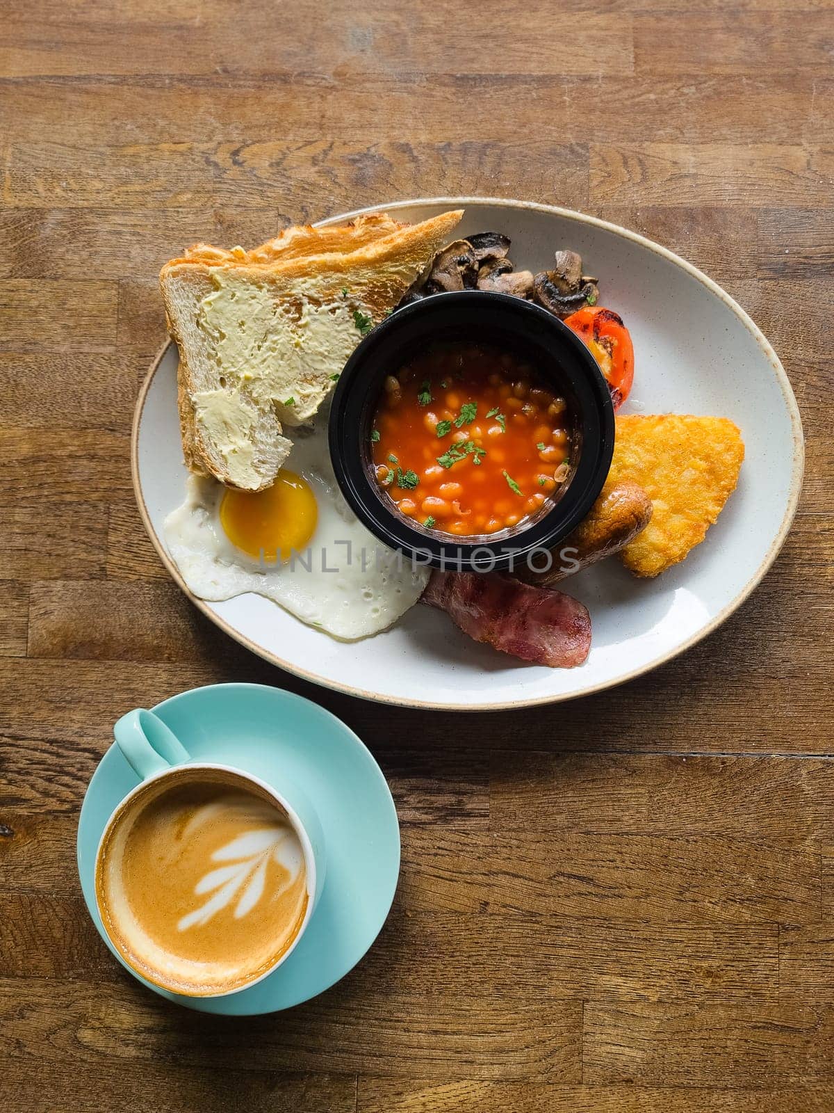 Full English breakfast with beans and sausage served on wooden table in pub