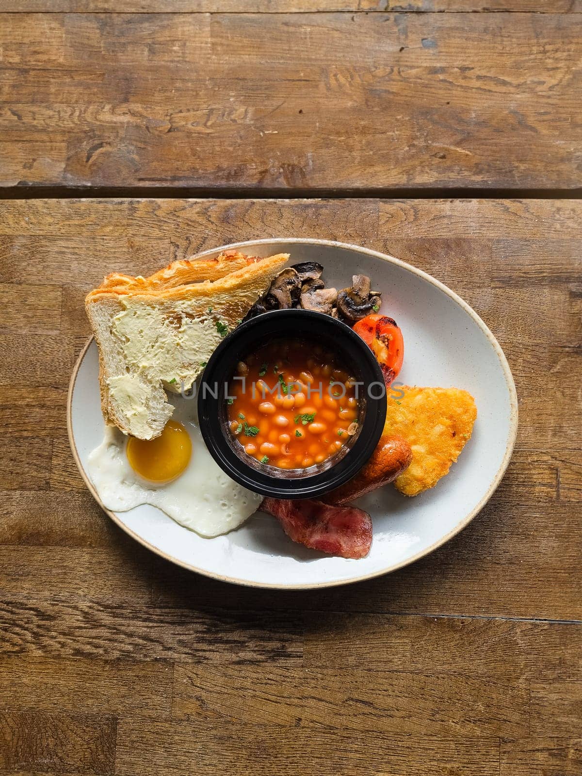 Full English breakfast with beans and sausage served on wooden table by Suteren
