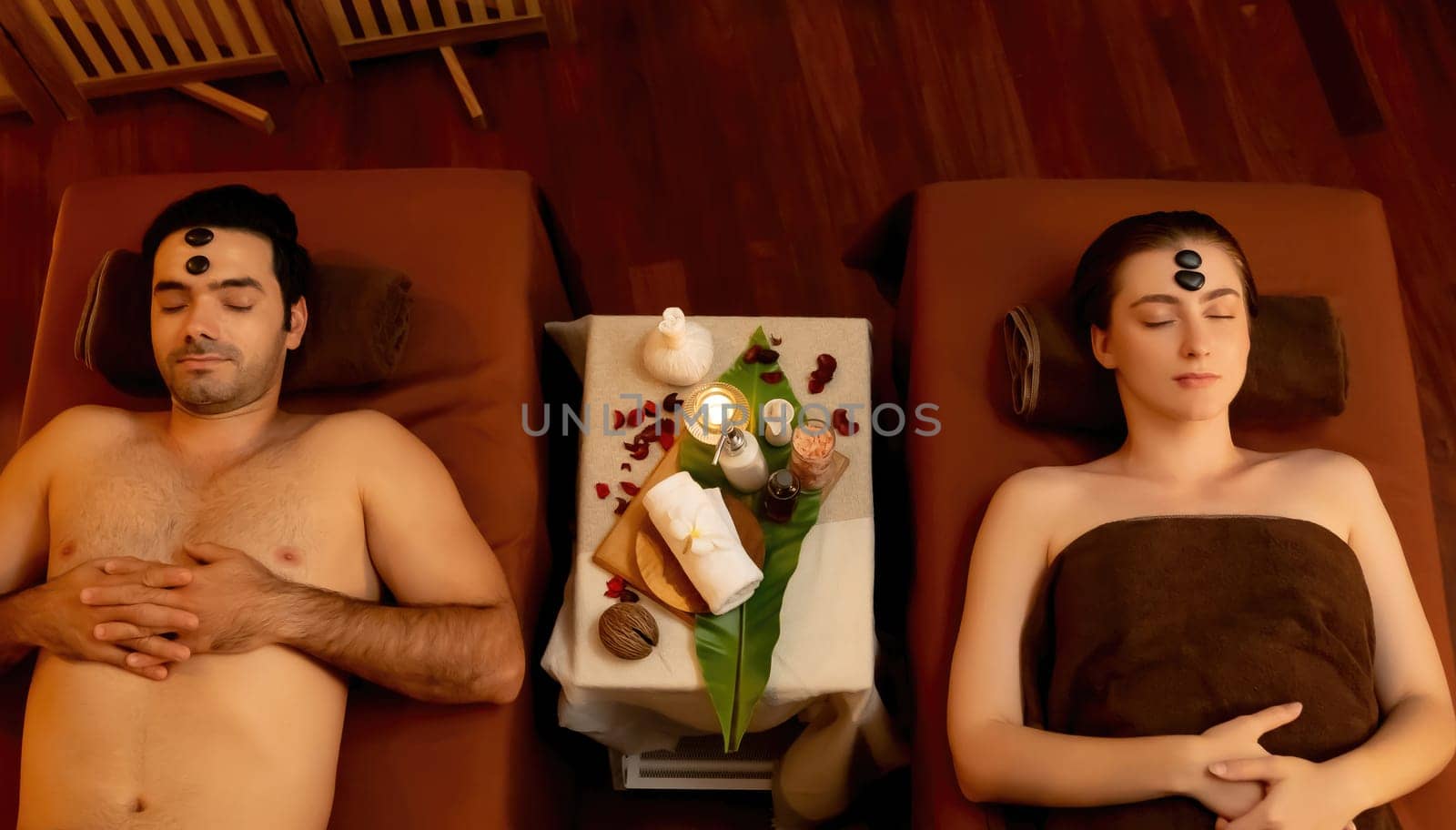 Top view couple enjoying relaxing anti-stress head massage with hot stone and pampering facial beauty skin recreation leisure in warm candle light ambient salon spa in resort or hotel. Quiescent