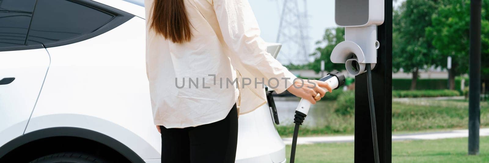 Young woman recharge EV car battery at charging station. Expedient by biancoblue