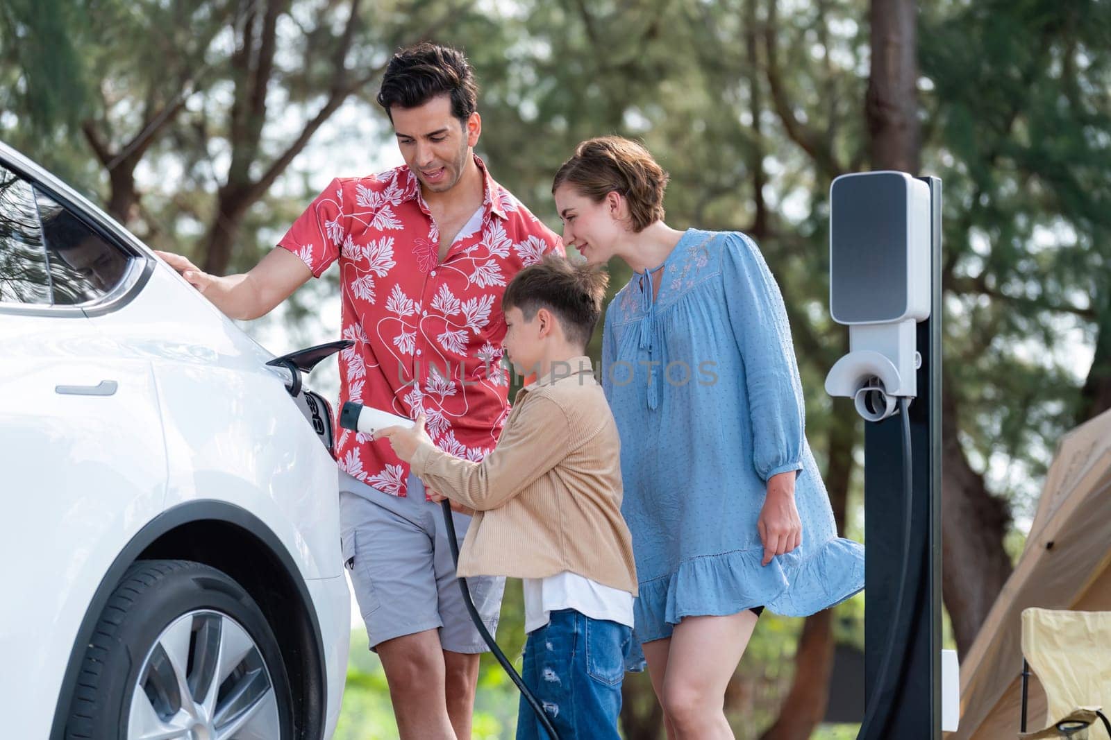 Outdoor adventure and family vacation camping in nature travel by eco friendly car for sustainable future. Lovely family recharge EV car with EV charging station in campsite. Perpetual