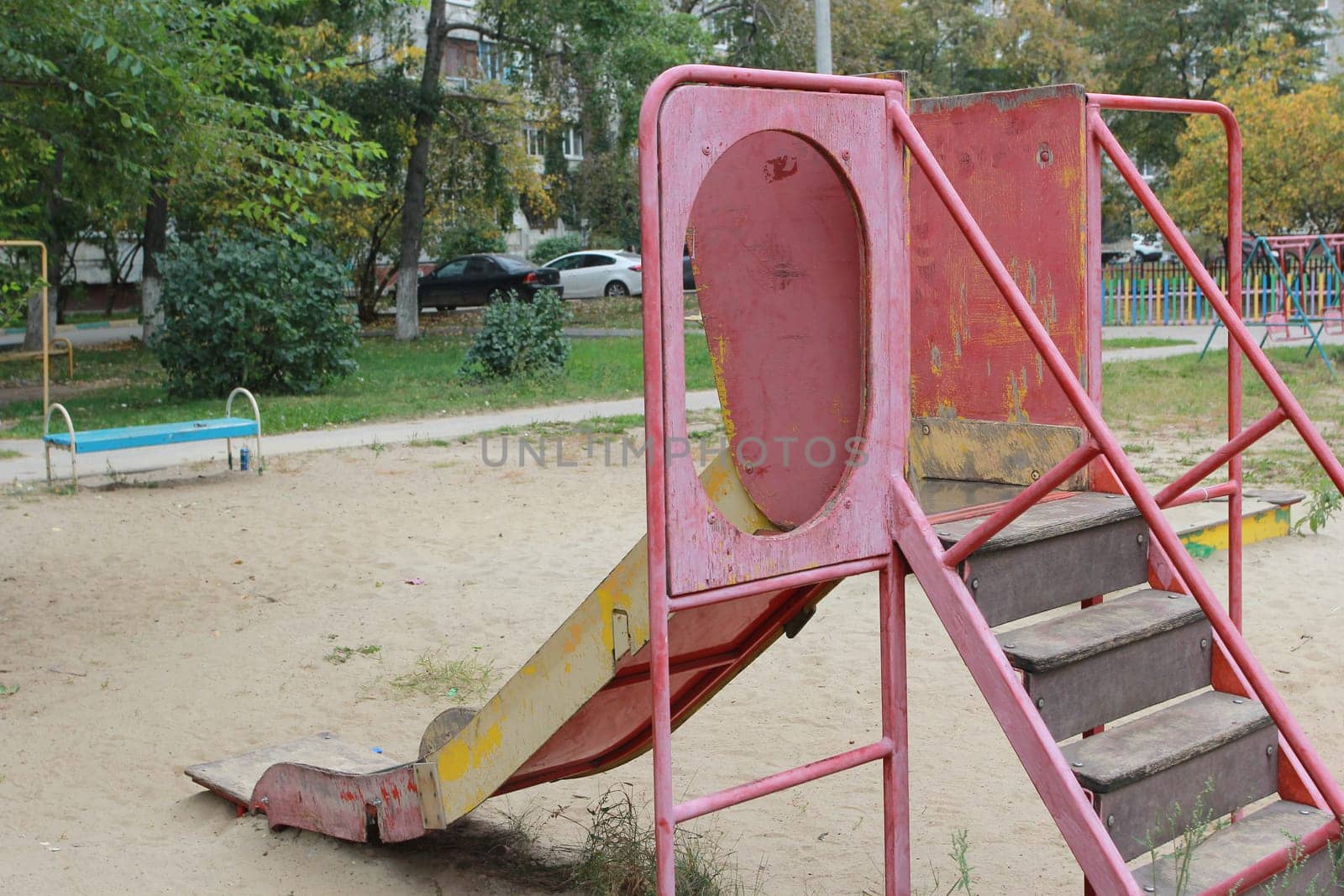 An old playground with a pink metal slide . Sand covering of the playground.