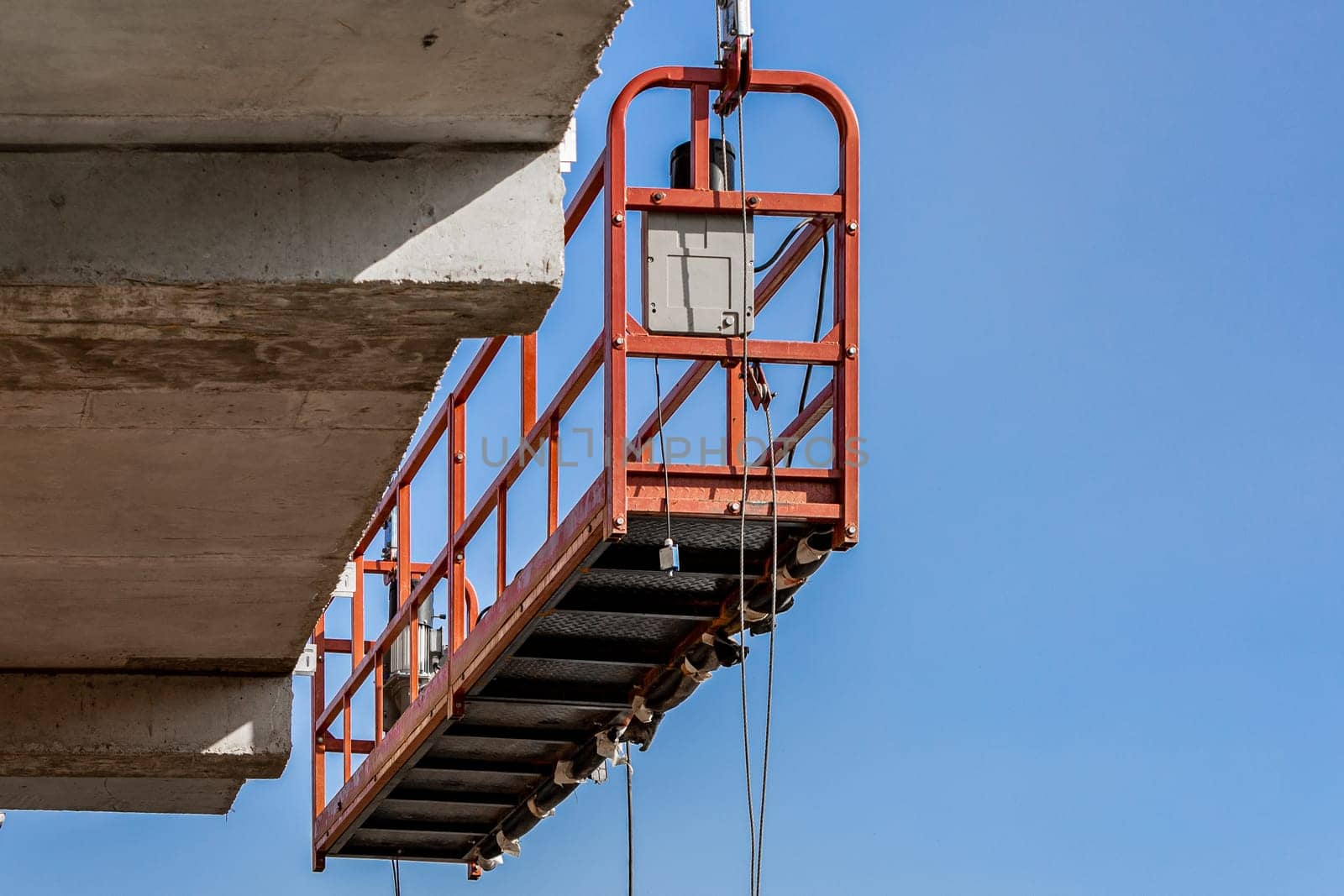 A lifting cradle at a construction site hangs on the monolithic frame of a new building under construction.