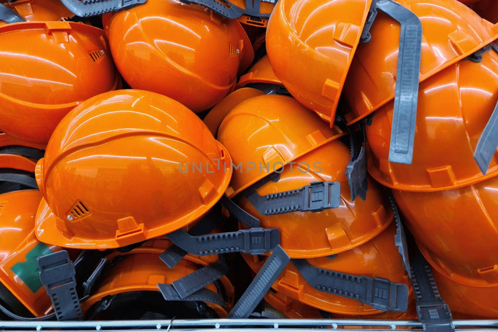 Many orange construction helmets lie on top of each other in a pile. Construction safety worker equipment.