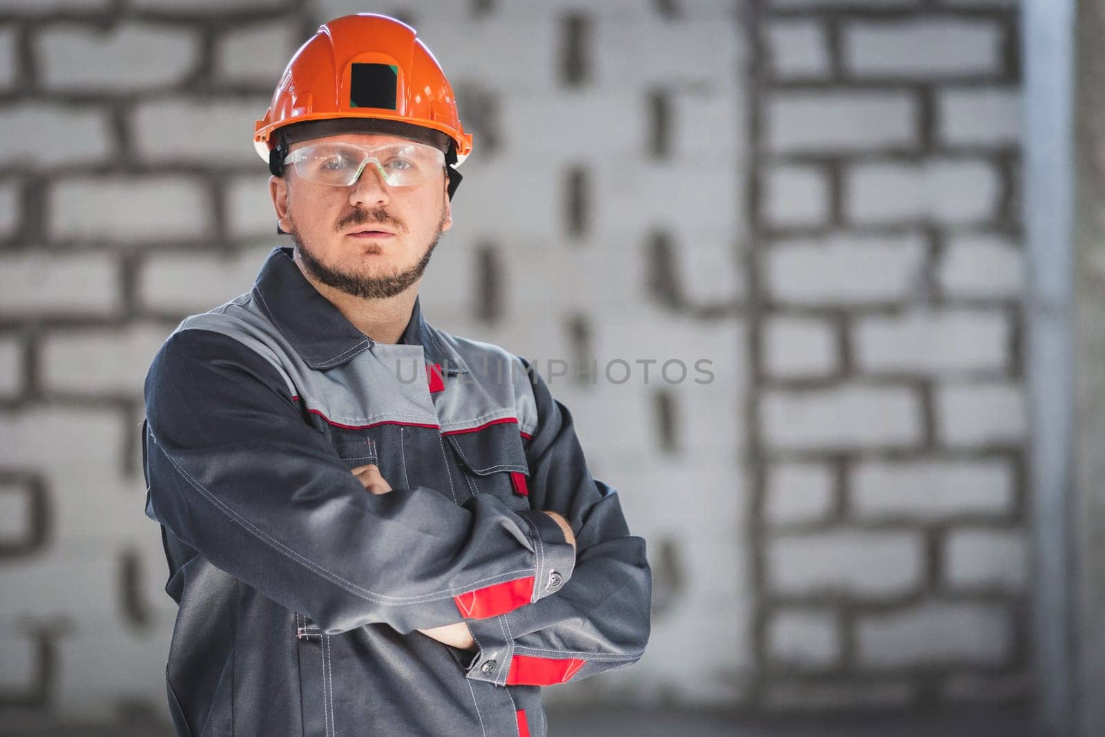 Bearded caucasian construction worker in uniform, safety helmet and safety glasses at a construction site, copy space