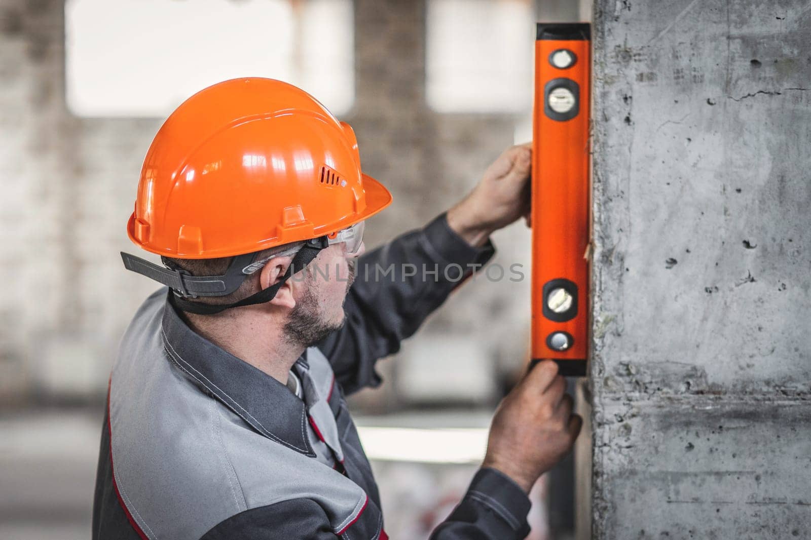 Construction worker man in a hard hat and overalls checks the vertical level of a reinforced concrete frame in new apartment.