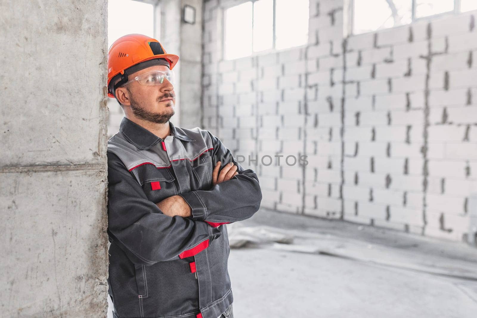 Worker in hard hat and protective glasses at a construction site near a reinforced concrete column, looking to the side, copy space.