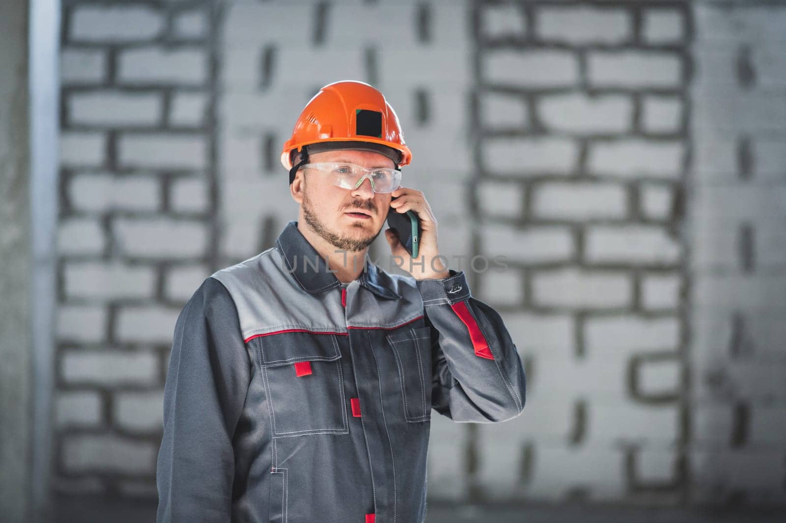 Caucasian male builder in overalls and helmet speaks on a cell phone.