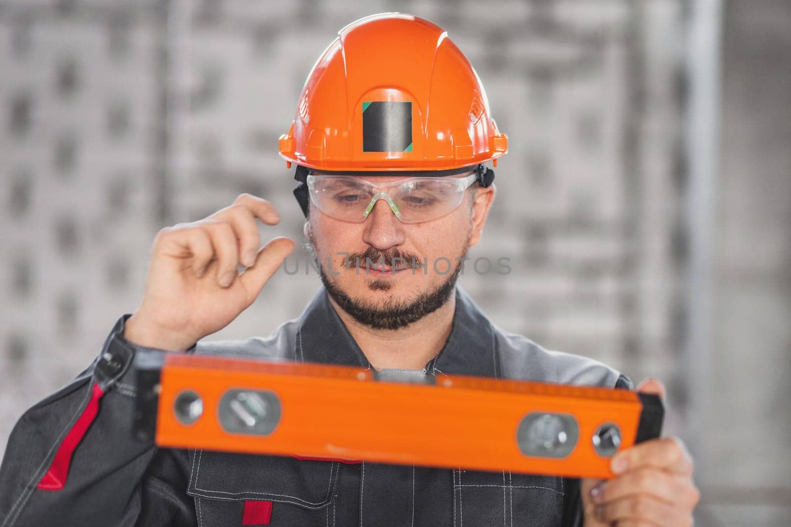 Construction worker portrait with level tool, caucasian bearded man in hard hat, protective glasses and uniform, building and inspection.