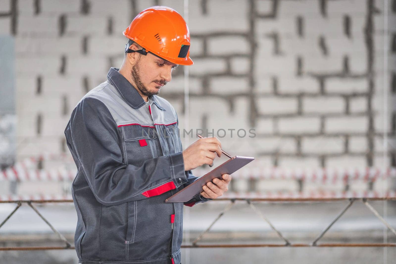 Caucasian worker at a construction site uses a digital tablet in his professional activities, copy space.