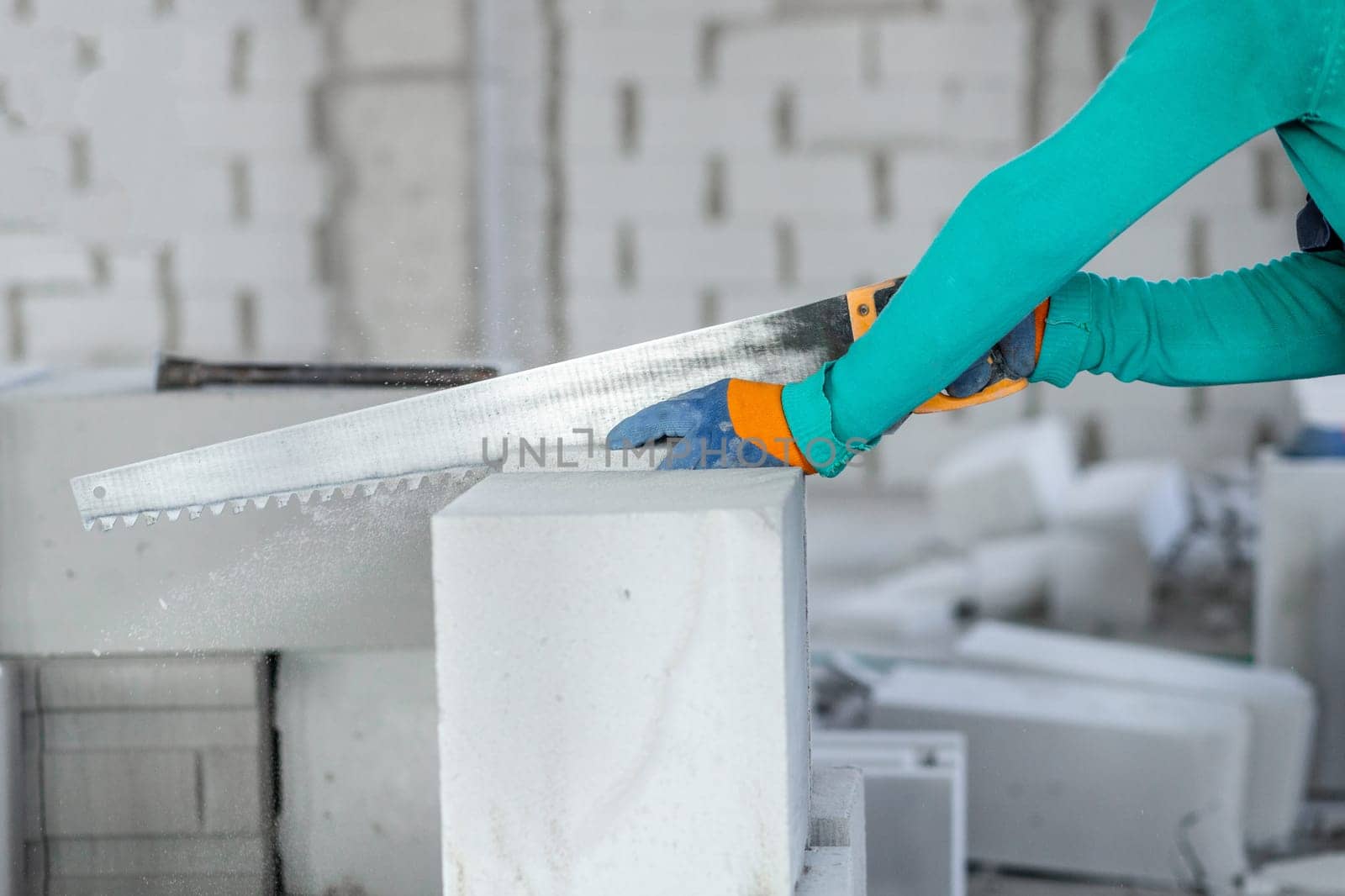 Sawing an autoclaved aerated gas block with a hand saw at a construction site during the construction of internal partitions of a building by Rom4ek