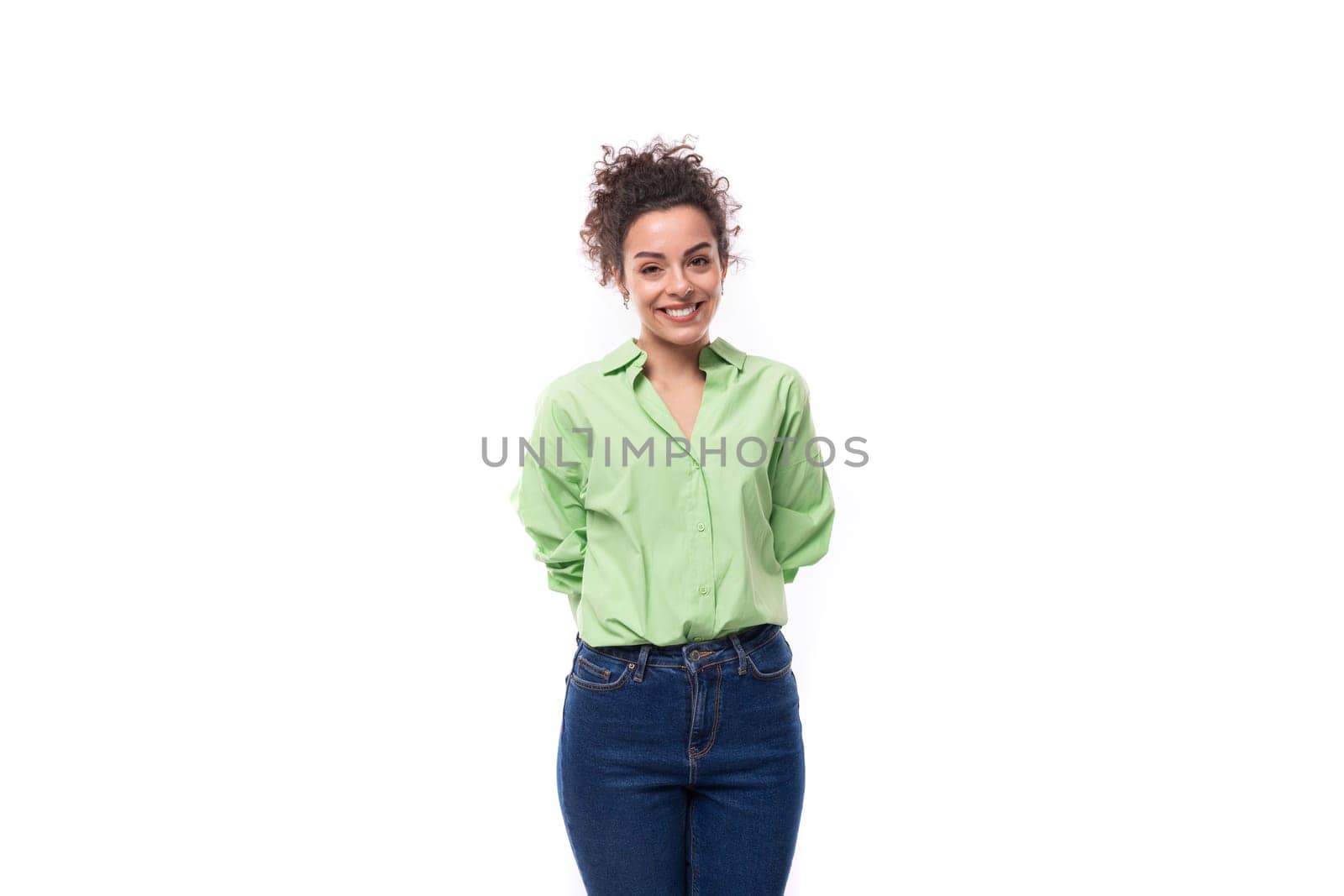 charming young brunette curly woman with a ponytail hairstyle is dressed in a green shirt and jeans.