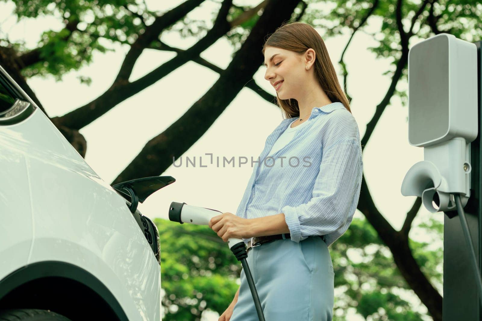 Young woman recharging battery for electric car during road trip. Exalt by biancoblue