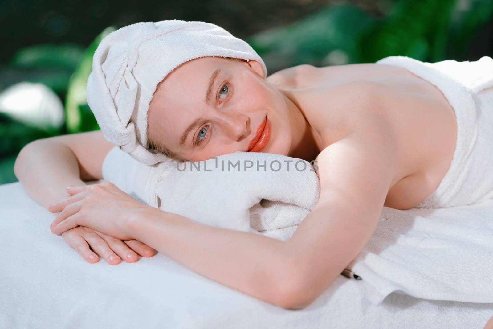 Beautiful young woman relaxes on a spa bed surrounded by nature. ready for a body massage. Attractive female in white towel lying peacefully during waiting for body massage. Close up. Tranquility