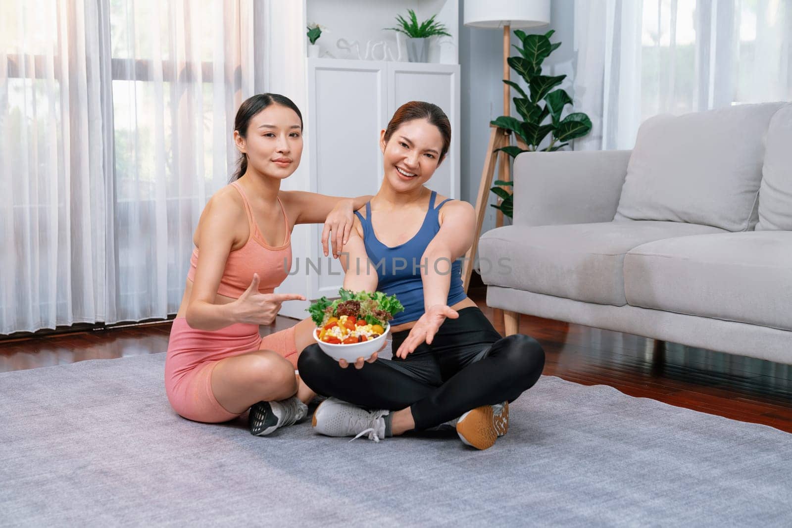 Young sporty Asian women in sportswear holding salad bowl together fill with vibrant of fruit and vegetable. Natural youthful and fit body lifestyle with balance nutrition and home exercise. Vigorous