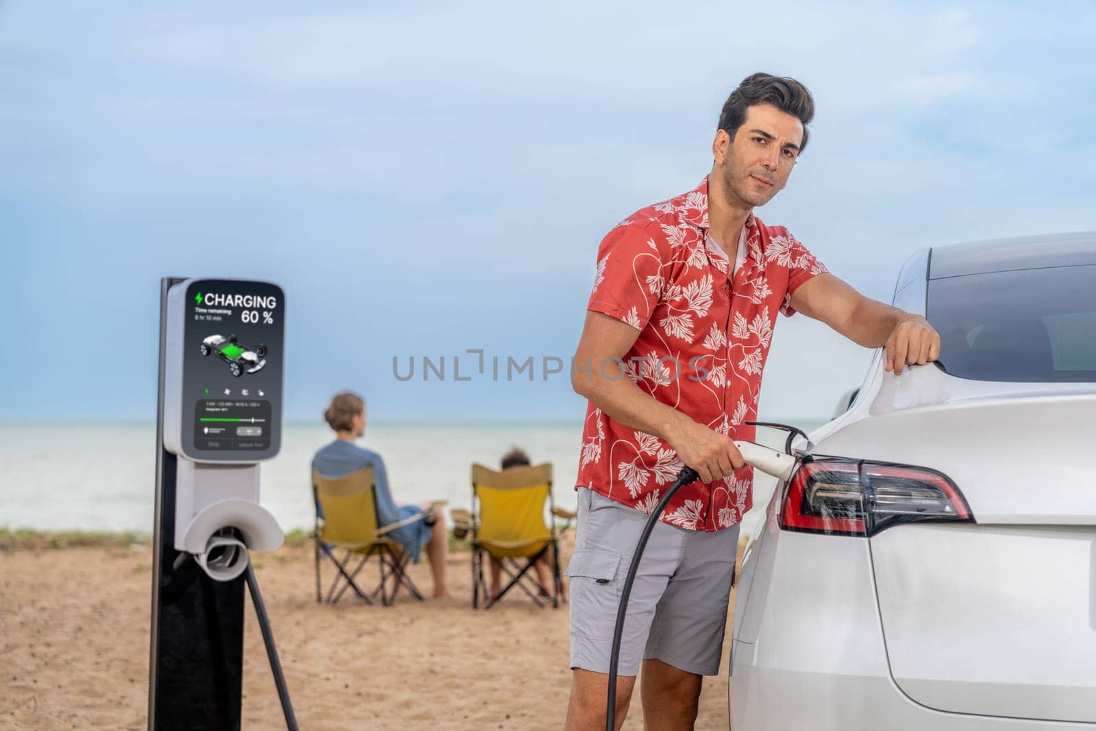 Family vacation trip traveling by the beach with electric car, dad or father recharge EV car while his family enjoy seascape beach. Family trip with alternative energy and eco-friendly car. Perpetual