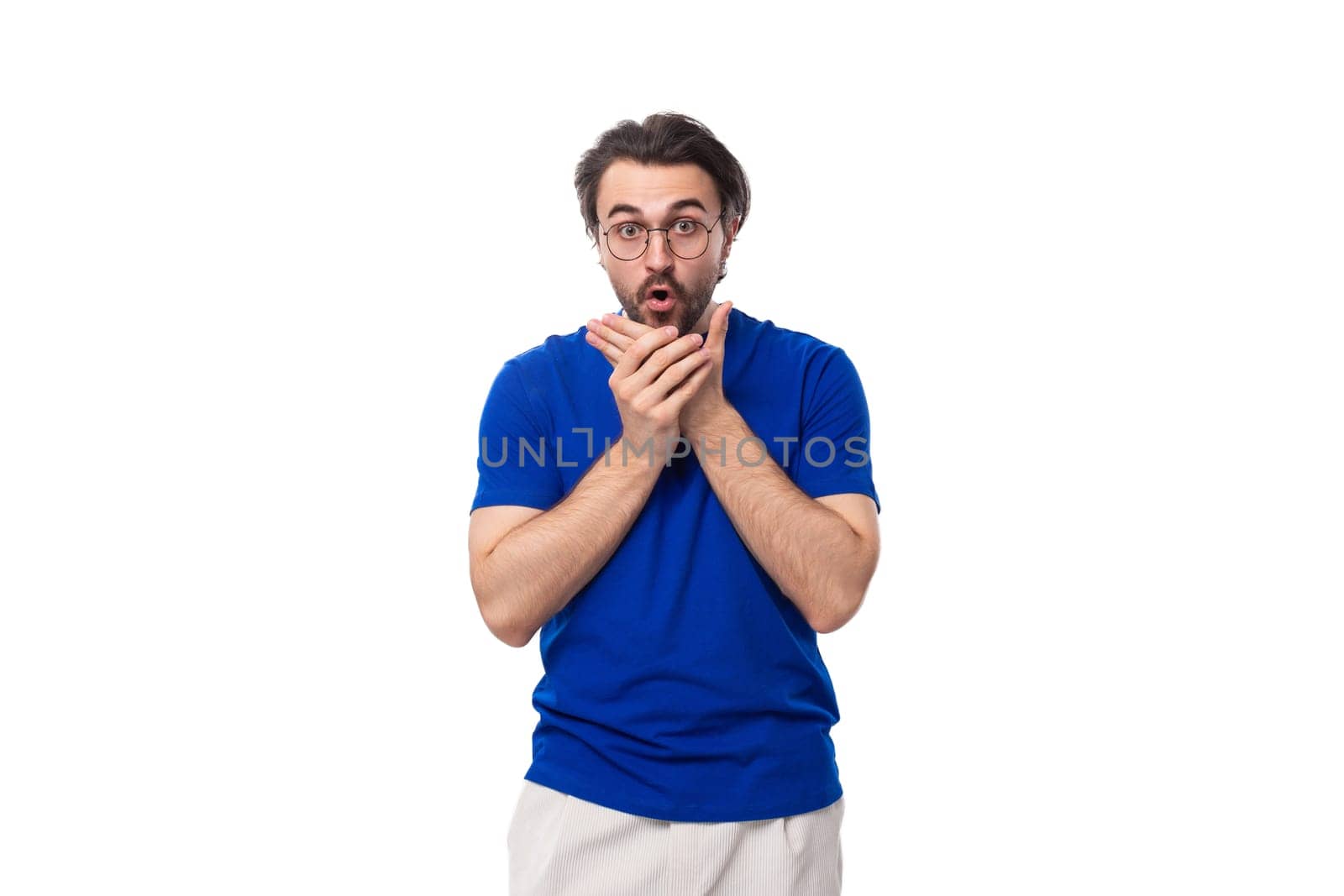30 year old surprised european brutal guy with black hair and a beard in a blue t-shirt on a white background with copy space by TRMK