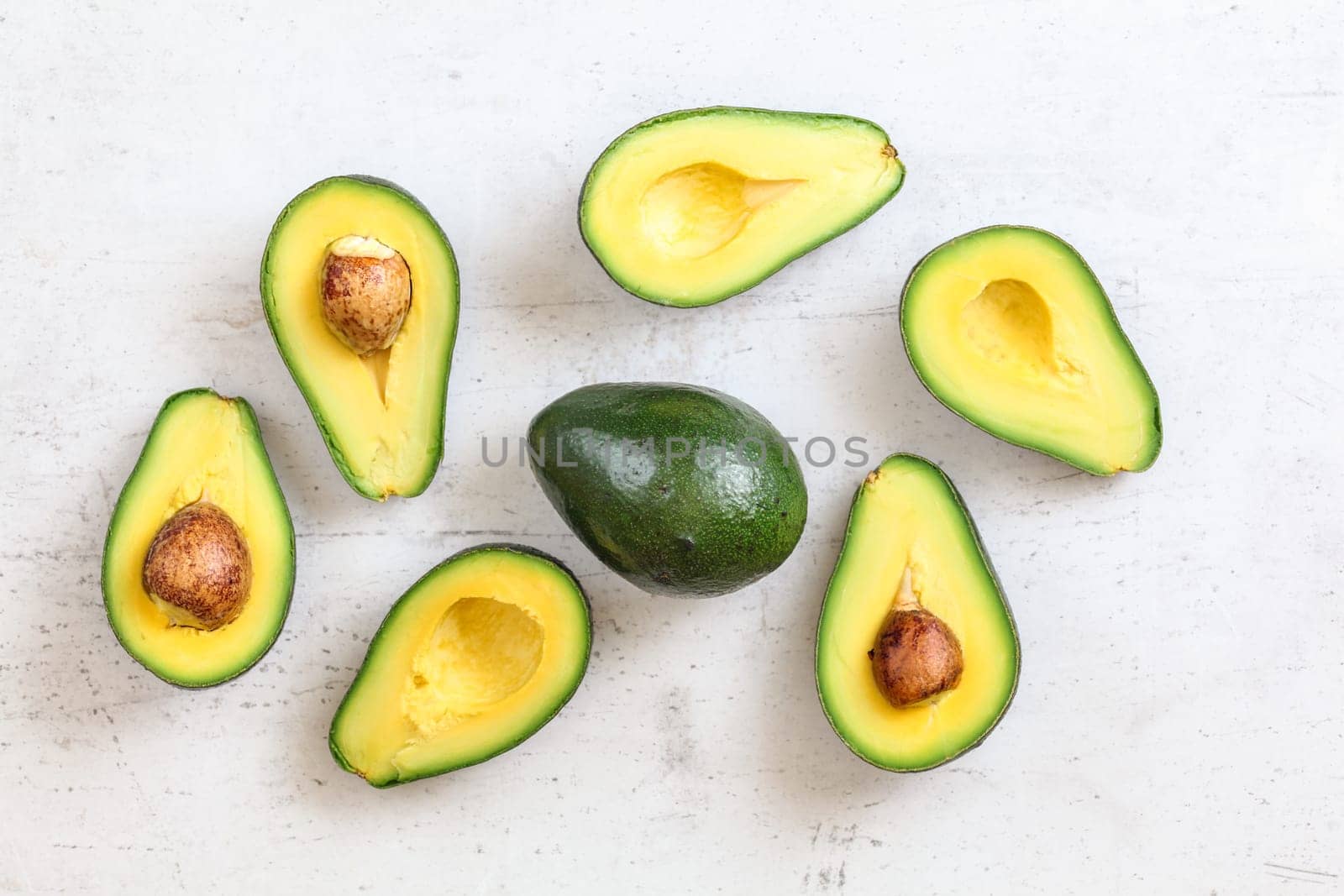 Overhead shot - avocados halves, some with seed, whole green pear in middle, on white working board. by Ivanko