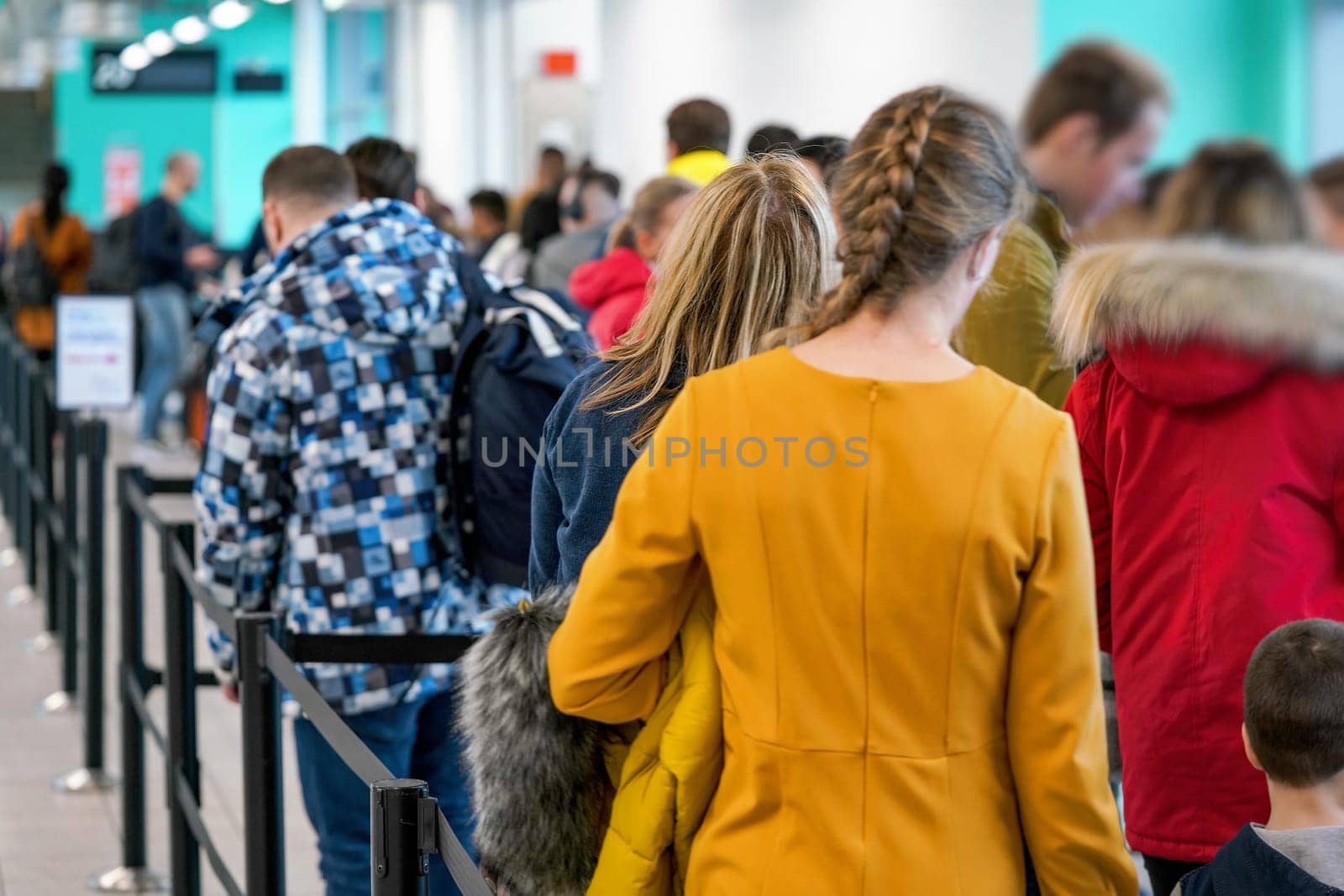 Group of anonymous people waiting at airport gate line to board an airplane, queue crowd seen from behind. by Ivanko