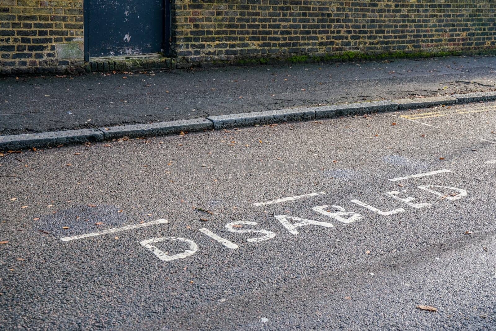 Word DISABLED written on asphalt near reserved parking space at street in outer London by Ivanko