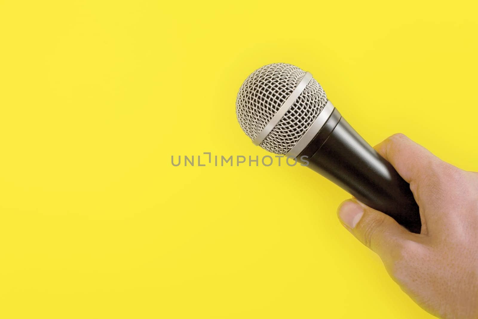 Man hand holds microphone, yellow background, space for text/image left by Ivanko