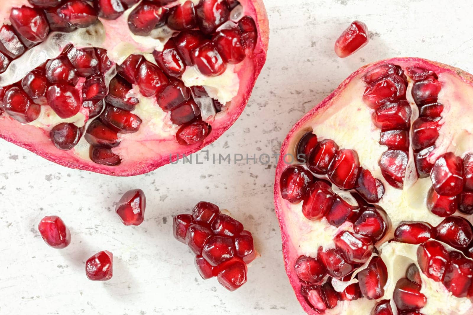 Pomegranate halves, gem like fruits scattered on white board, photo from above.