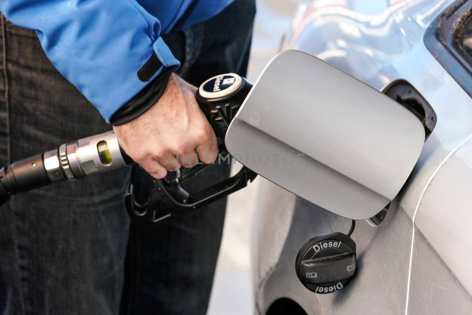 Man refilling gas tank of his silver diesel car. Detail on opened cover.