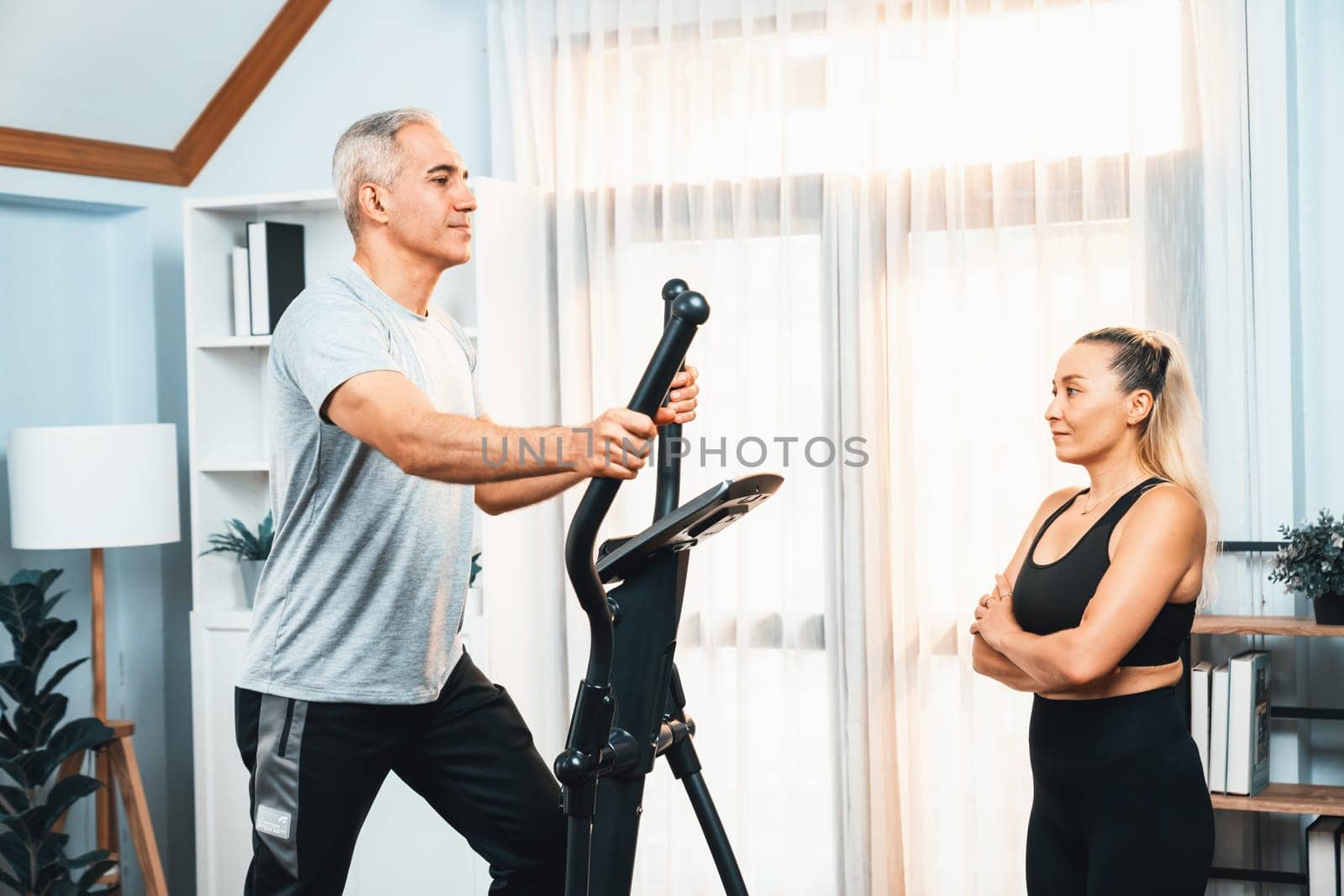 Active senior couple running on elliptical running machine at home together as fitness healthy lifestyle and body care after retirement for pensioner. Clout