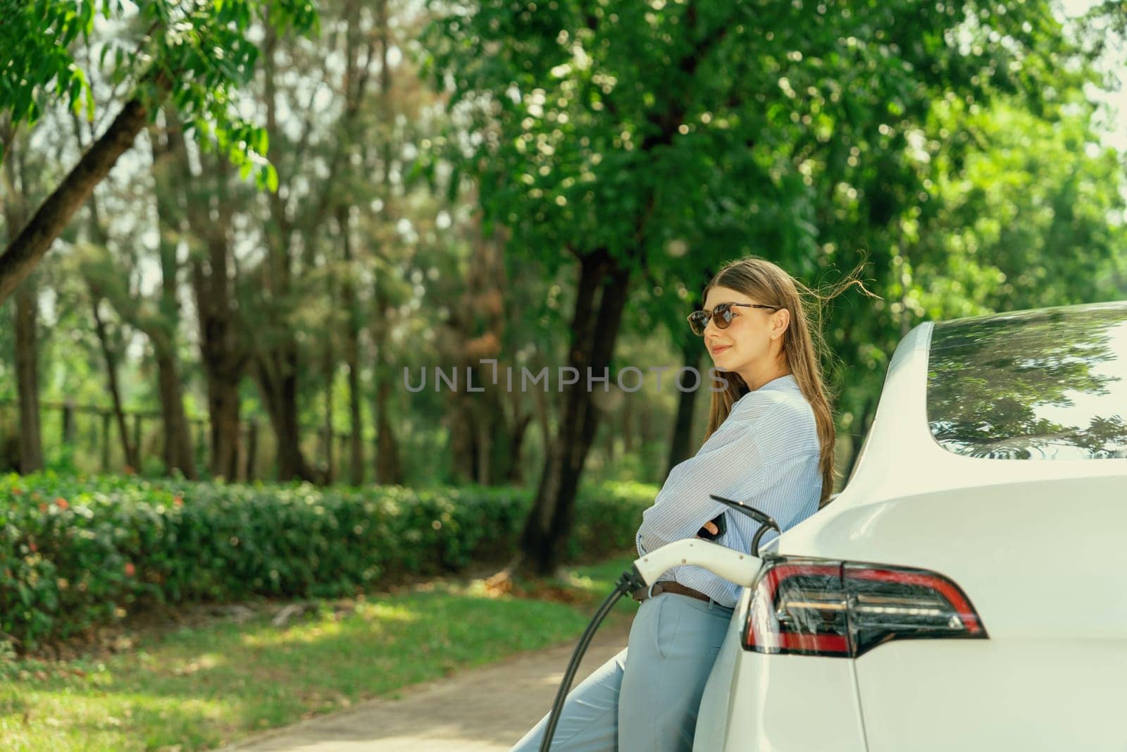 Young woman using smartphone to pay for electric car charging. Exalt by biancoblue