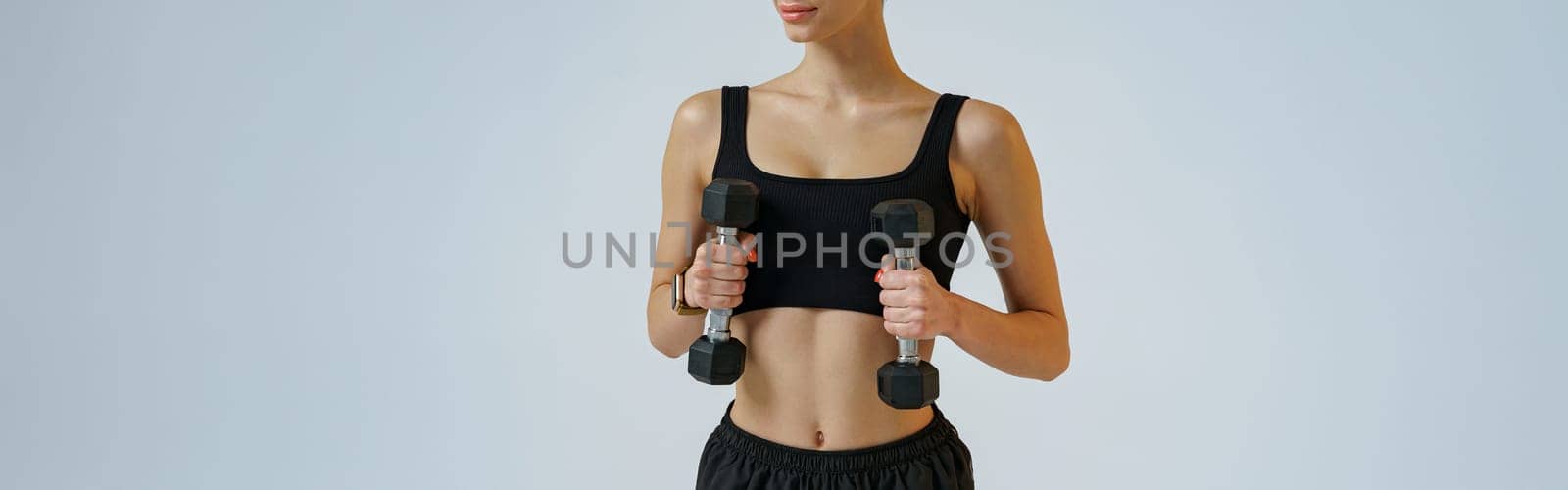 Attractive fitness woman doing exercises with dumbbells on studio background and looking at side by Yaroslav_astakhov