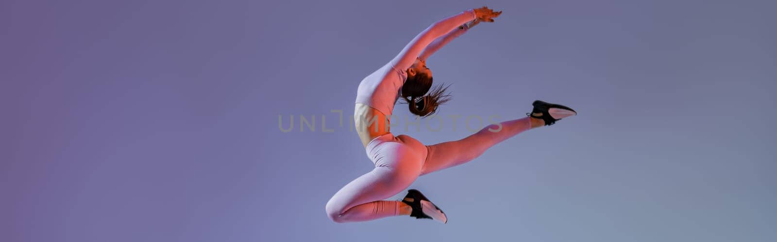 Athletic active woman jumping on studio background with colored filter. Dynamic movement