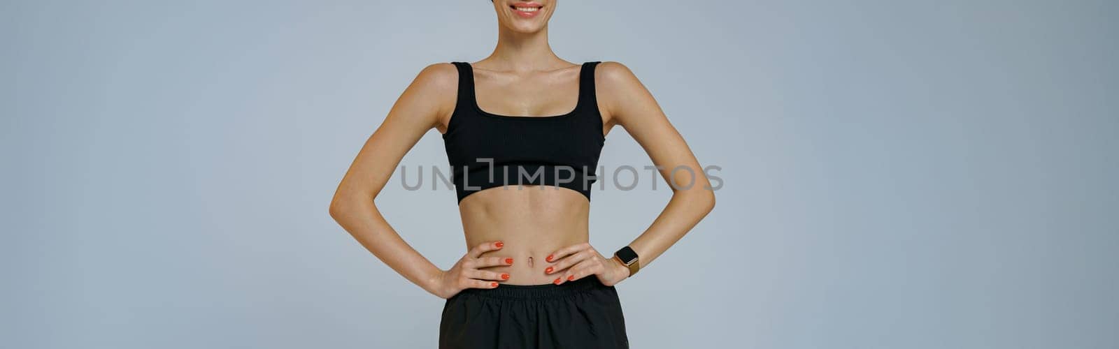 Portrait of smiling fitness woman wearing sportswear looking at camera on studio background by Yaroslav_astakhov