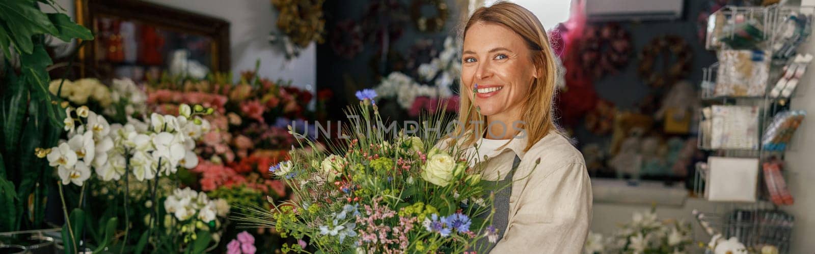 Attractive woman flower shop owner in apron holding bouquet of flowers at florist store