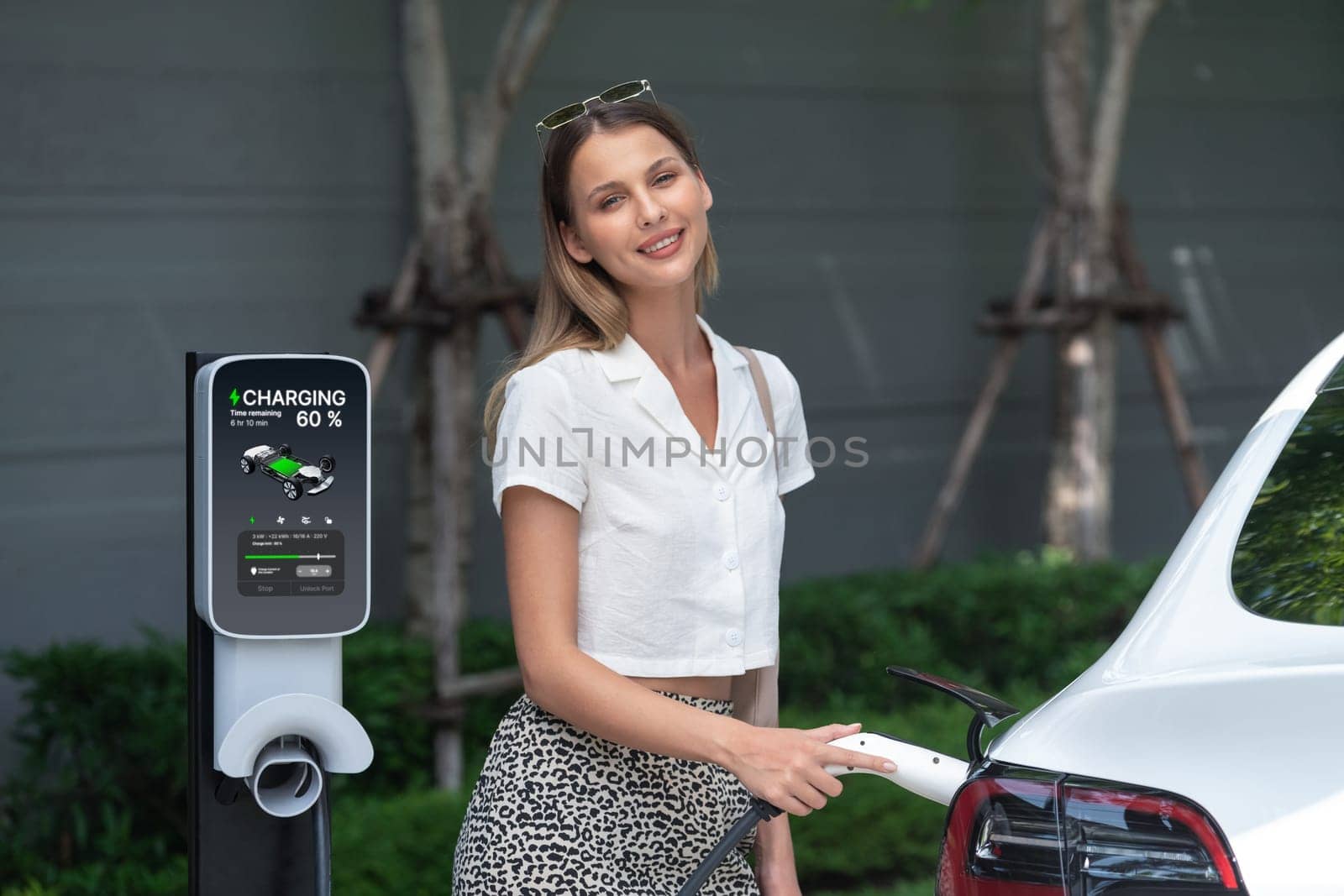 Young woman travel with EV electric car charging in green sustainable city outdoor garden in summer. Urban sustainability lifestyle by green clean rechargeable energy of electric BEV vehicle innards