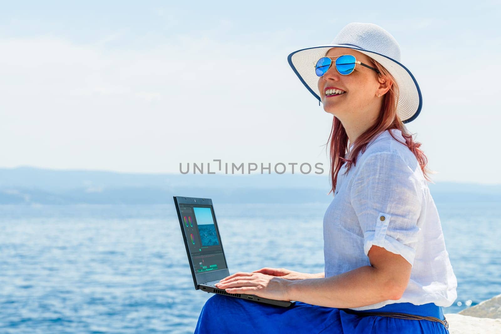 Freelancer girl working on laptop while enjoying vacation at the seaside beach by PhotoTime